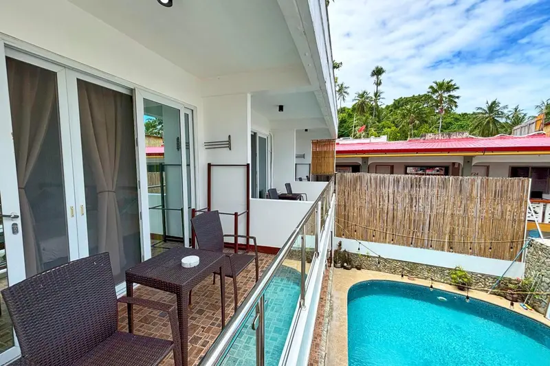 Une terrasse avec mobilier en osier donne sur une piscine et une végétation luxuriante.