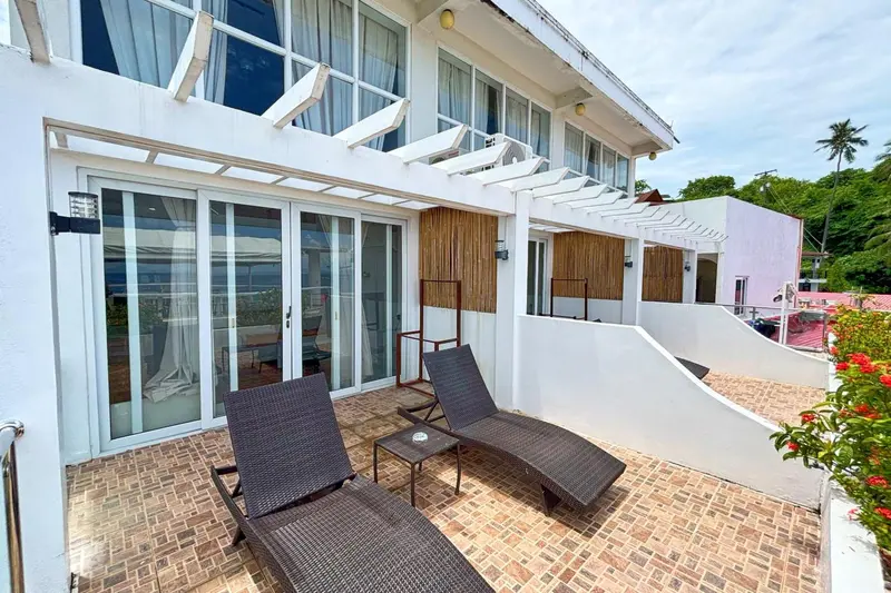 Terrasse carrelée avec transats et mobilier de jardin devant une façade blanche.