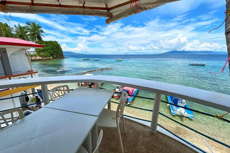 Une table et des chaises sont disposées sur une terrasse ombragée avec vue sur la mer.