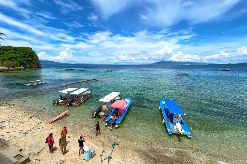 Plage de sable avec plusieurs bateaux à moteur ancrés dans une eau turquoise.