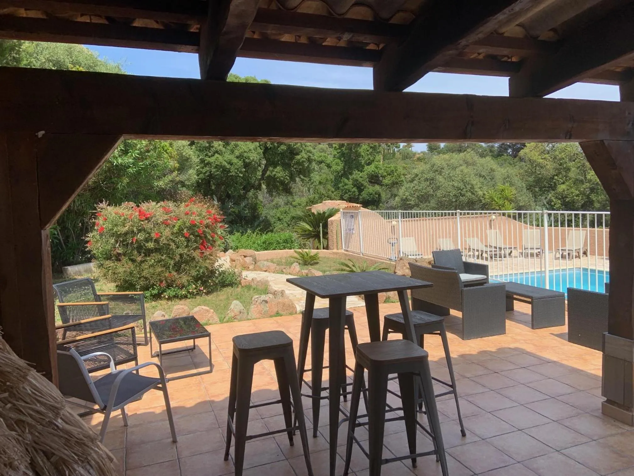 Terrasse ombragée avec tables et chaises donnant sur un jardin et une piscine.