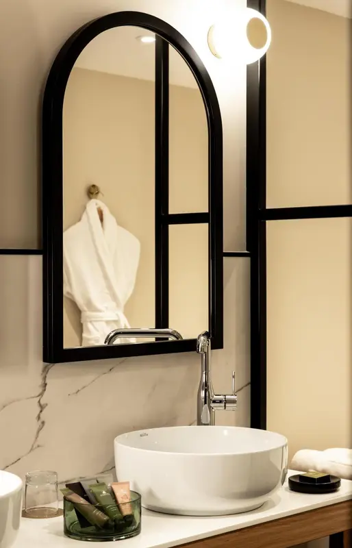 Un lavabo blanc et un grand miroir noir ornent une salle de bain lumineuse.