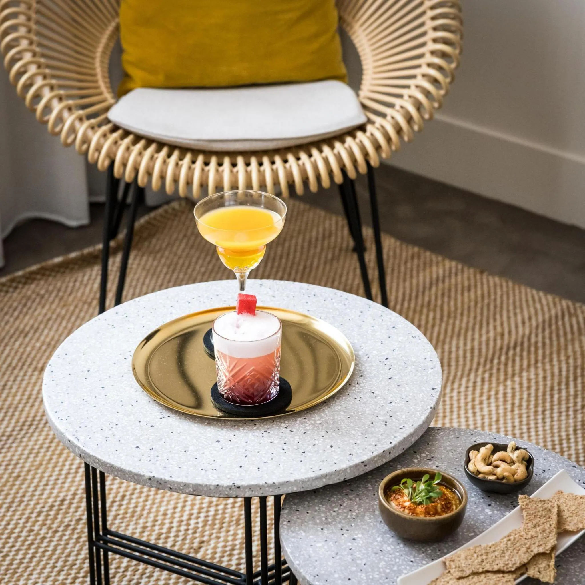 Un cocktail coloré et des amuse-gueules sont servis sur une table basse en terrasse.