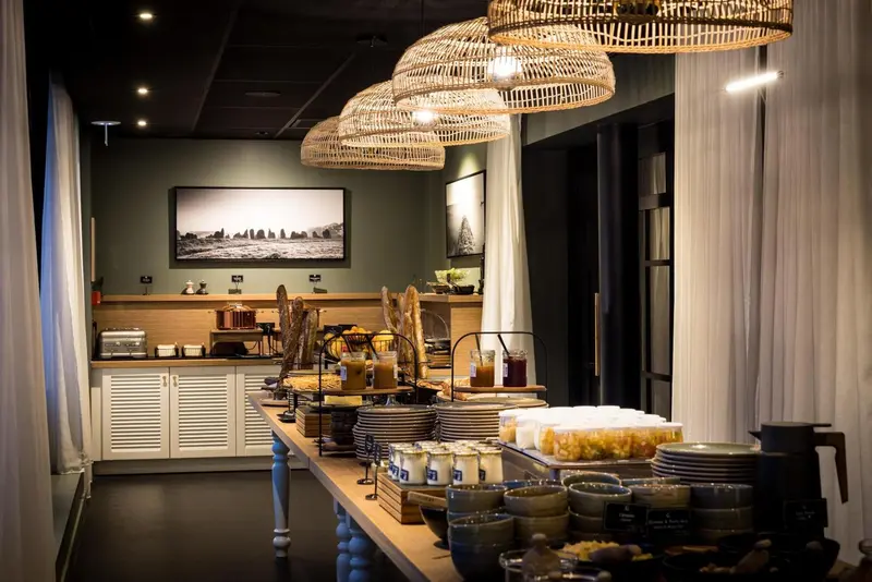 Un buffet propose une variété de pains, pâtisseries et fruits frais dans une salle lumineuse.