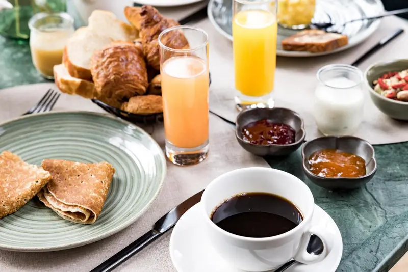 Une table est dressée avec un petit-déjeuner composé de viennoiseries, de fruits et de boissons.
