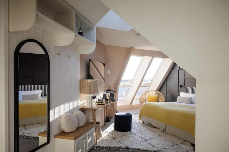 Chambre mansardée lumineuse avec un lit jaune et un miroir en arc de cercle.