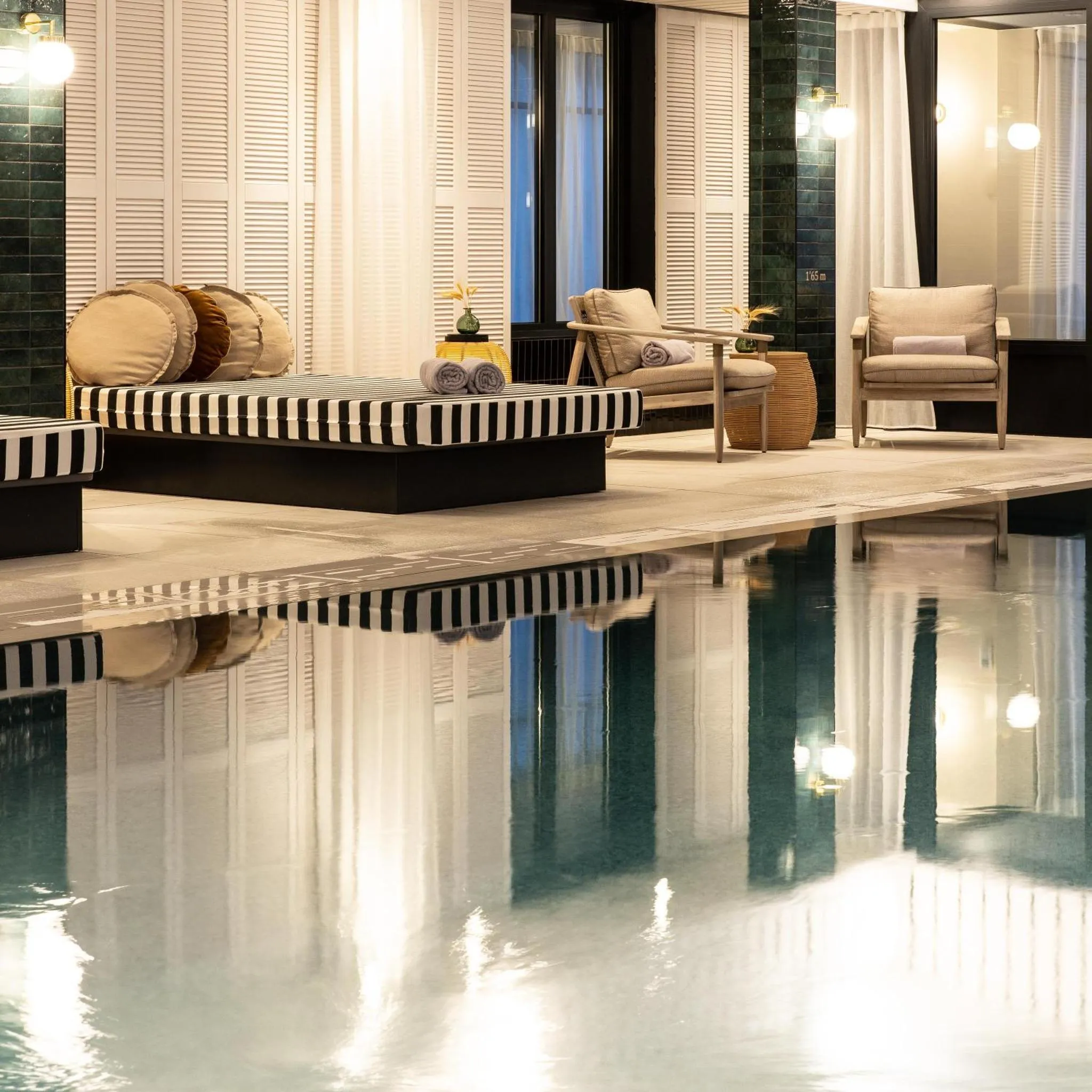 Espace de détente avec banquettes rayées et fauteuils près d'une piscine intérieure.