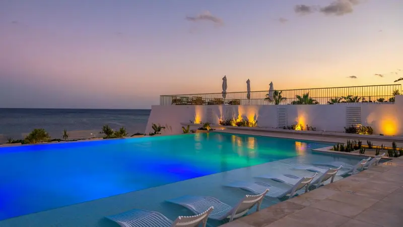 Piscine illuminée avec transats et vue sur la mer au coucher du soleil.