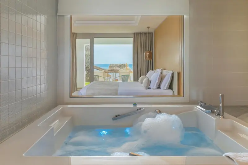 Une baignoire remplie d'eau mousseuse se trouve dans une salle de bain moderne avec vue sur la mer.