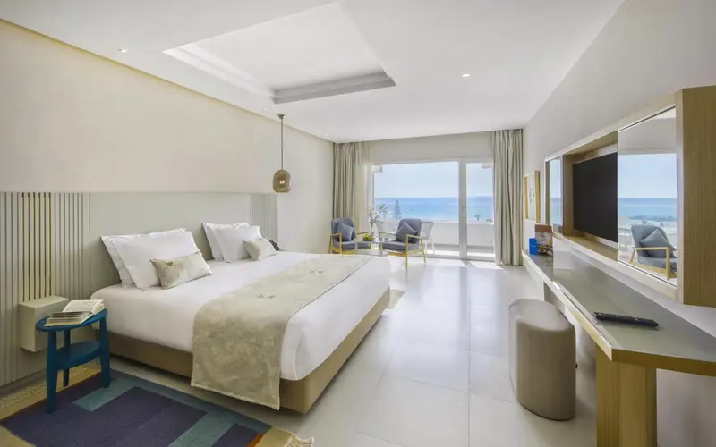 Chambre lumineuse avec un grand lit et une vue sur la mer.