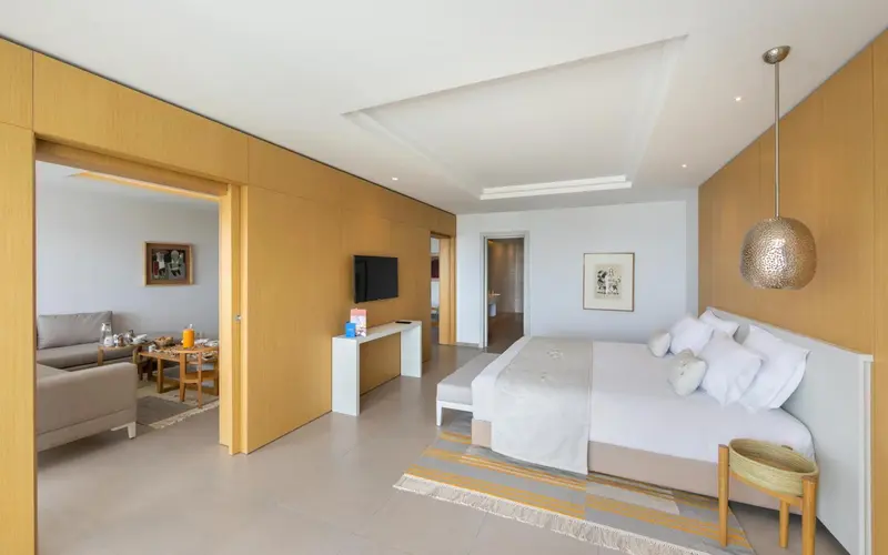 Chambre lumineuse avec un grand lit et un espace salon attenant.
