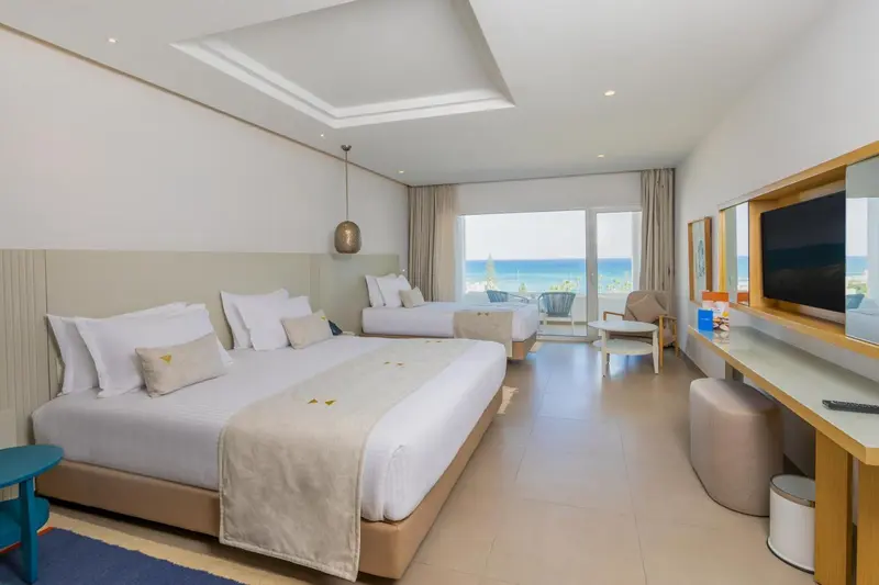 Chambre lumineuse avec deux lits simples et vue sur la mer.