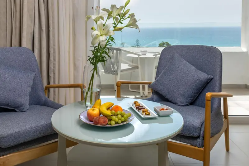 Une table basse avec des fruits frais se trouve devant deux fauteuils confortables avec vue sur la mer.