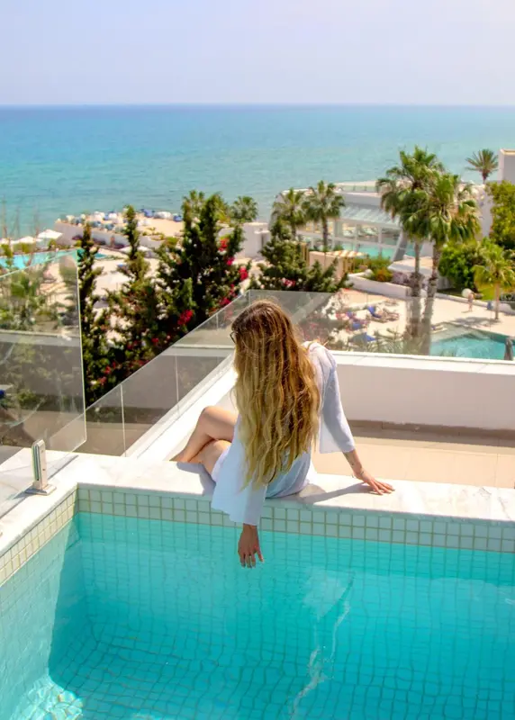 Une femme assise au bord d'une piscine avec vue sur la mer et la végétation.