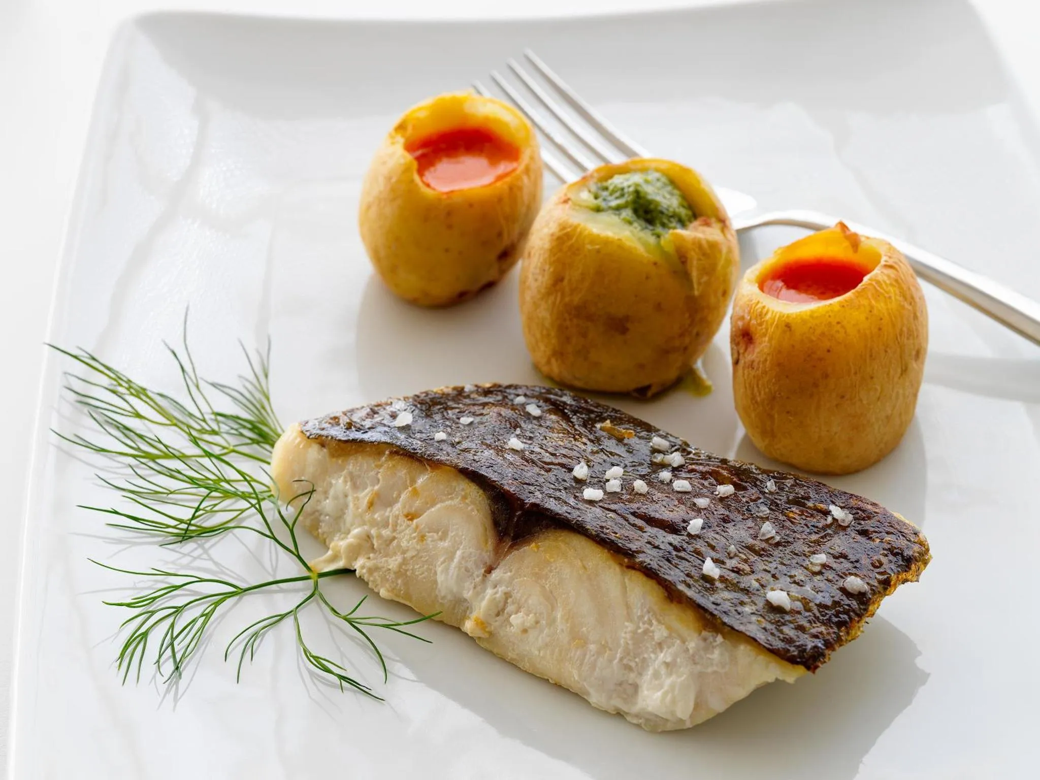 Un plat de poisson blanc servi avec des pommes de terre farcies et une garniture verte.