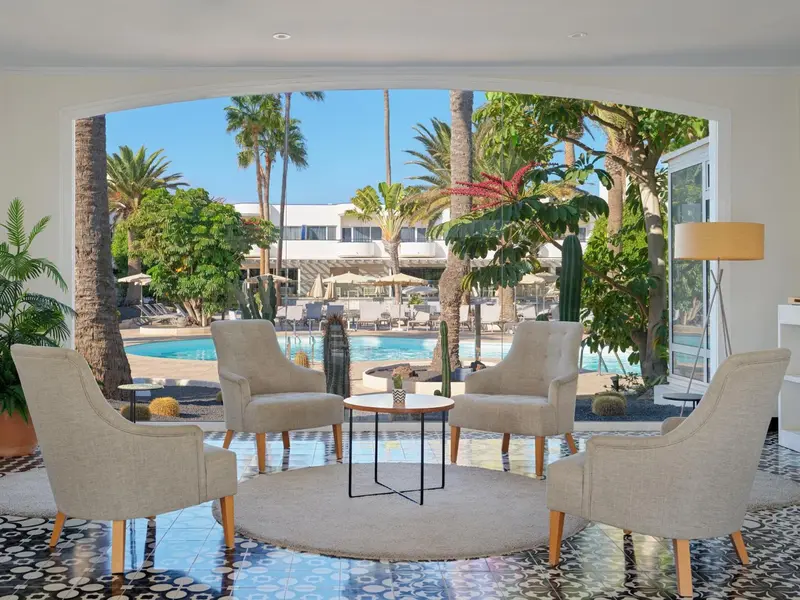 Un espace salon lumineux avec des fauteuils et une vue sur une piscine et une végétation tropicale.
