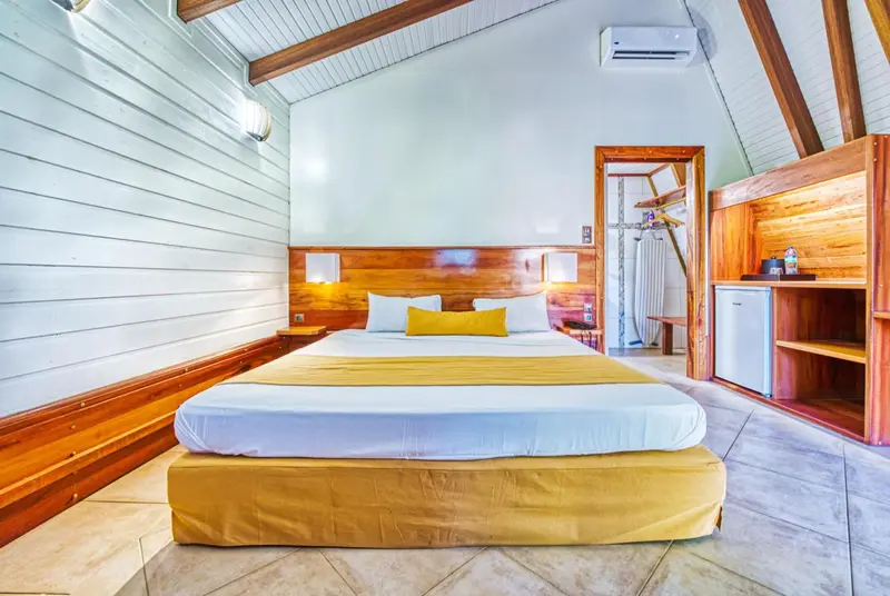 Une chambre lumineuse avec un grand lit recouvert d'un plaid jaune et de coussins.