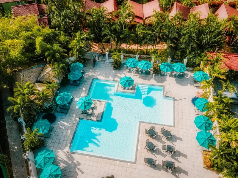 Vue aérienne d'une piscine turquoise entourée de transats sous des parasols bleus.