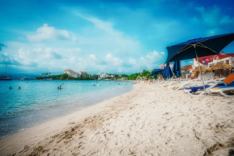 Plage de sable blanc bordée d'une eau turquoise sous un ciel bleu nuageux.
