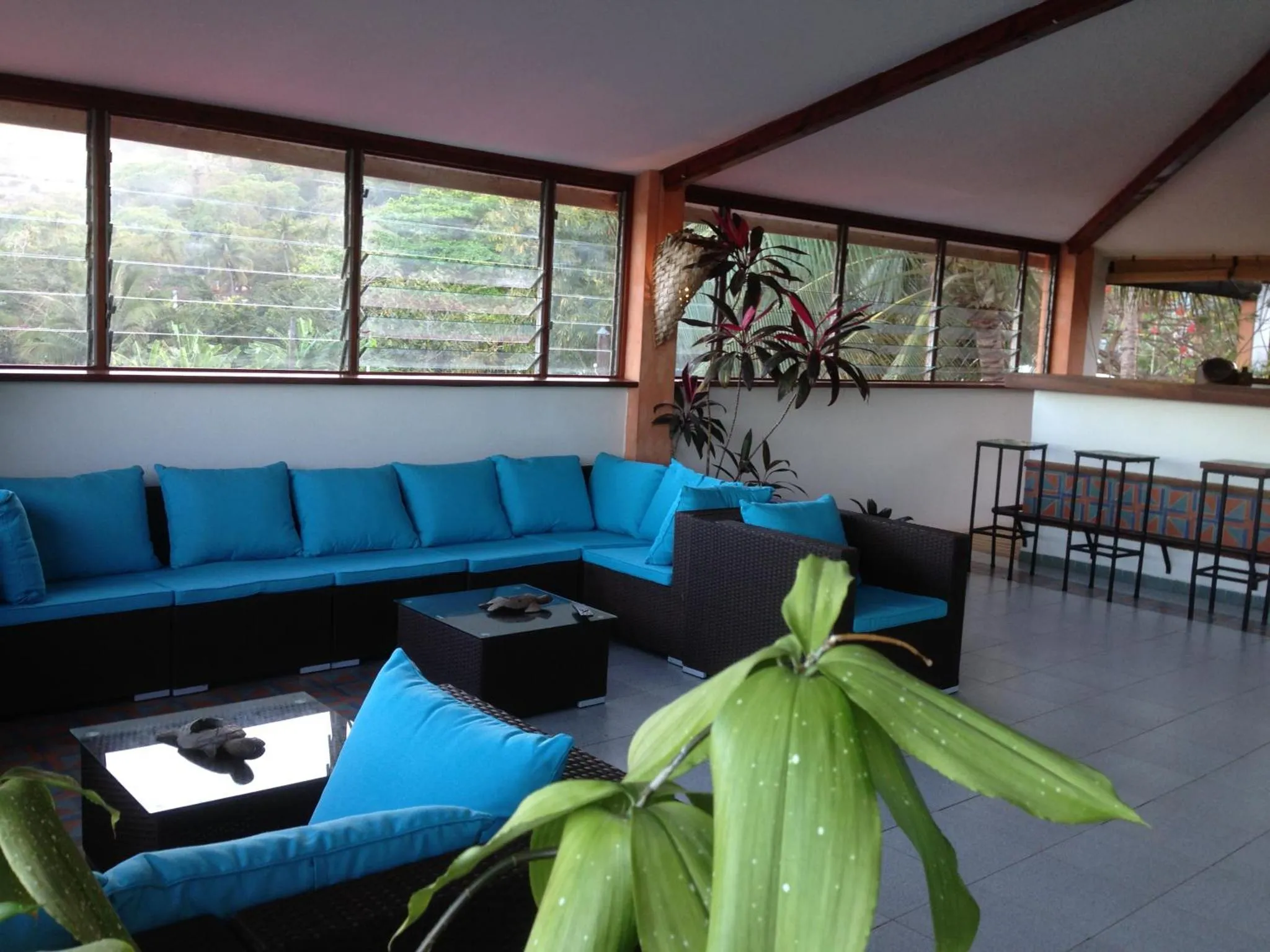 Espace de détente avec canapés bleus et mobilier en rotin.