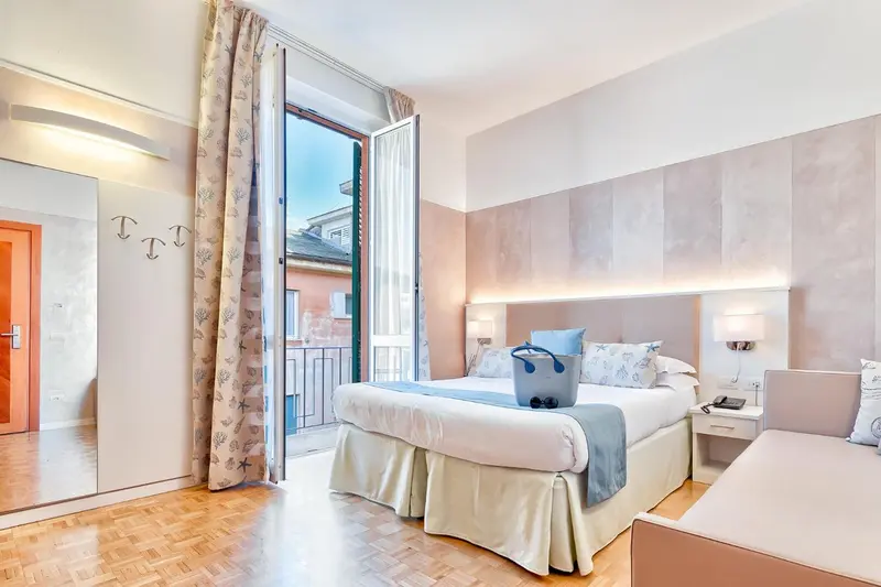 Chambre lumineuse avec un lit recouvert d'une courtepointe blanche et bleue, donnant sur un balcon.
