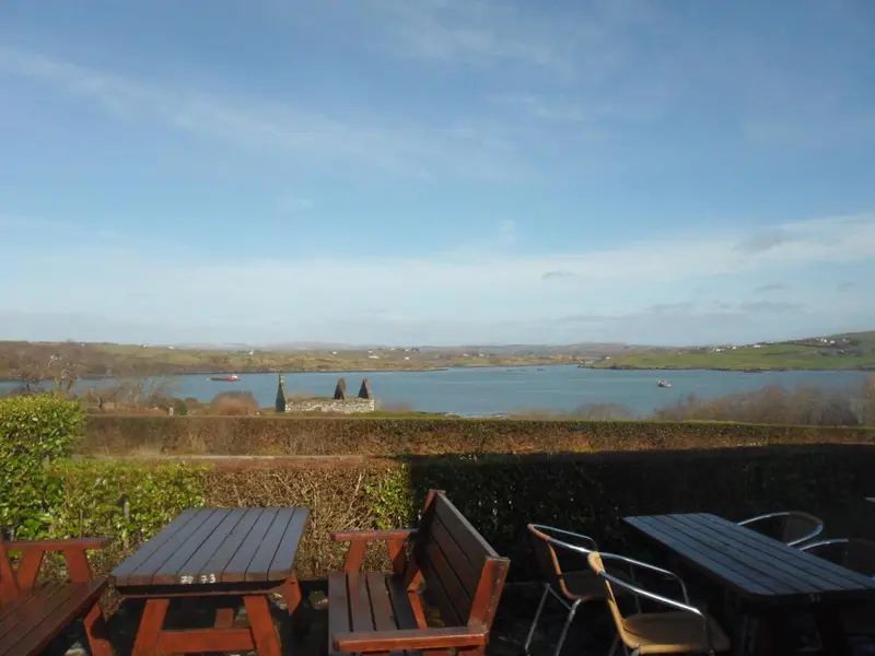 Terrasse avec tables et chaises donnant sur une baie et un paysage verdoyant.