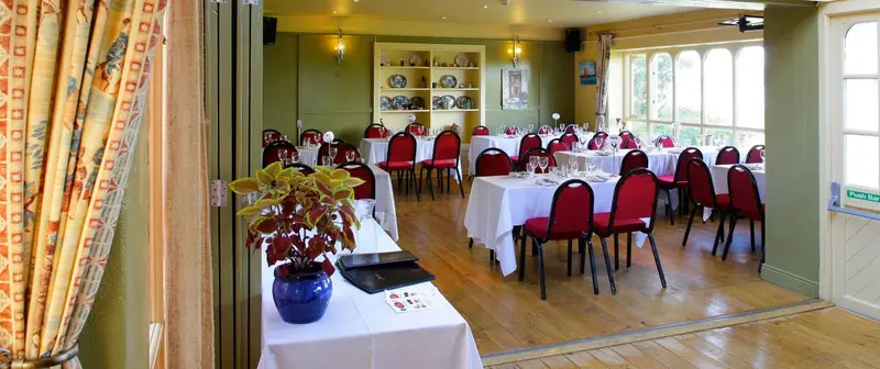 Une salle lumineuse est aménagée avec des tables dressées pour un repas.