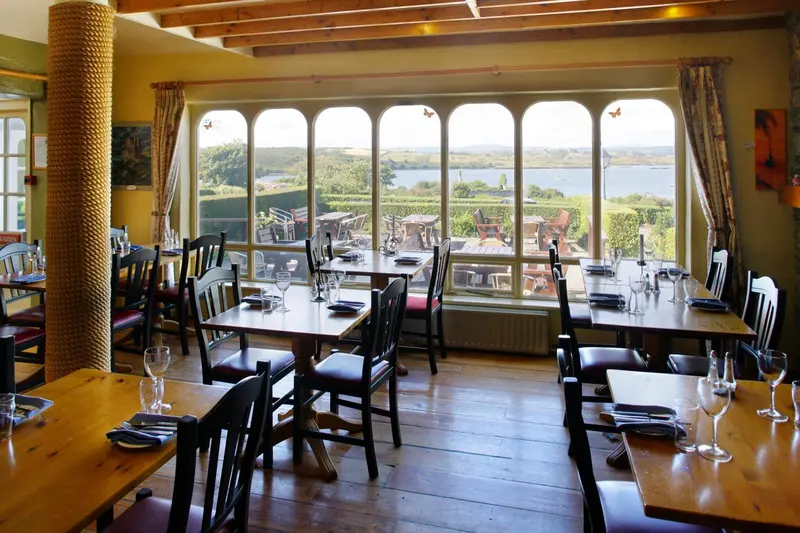 Une salle lumineuse avec des tables dressées face à un paysage verdoyant.