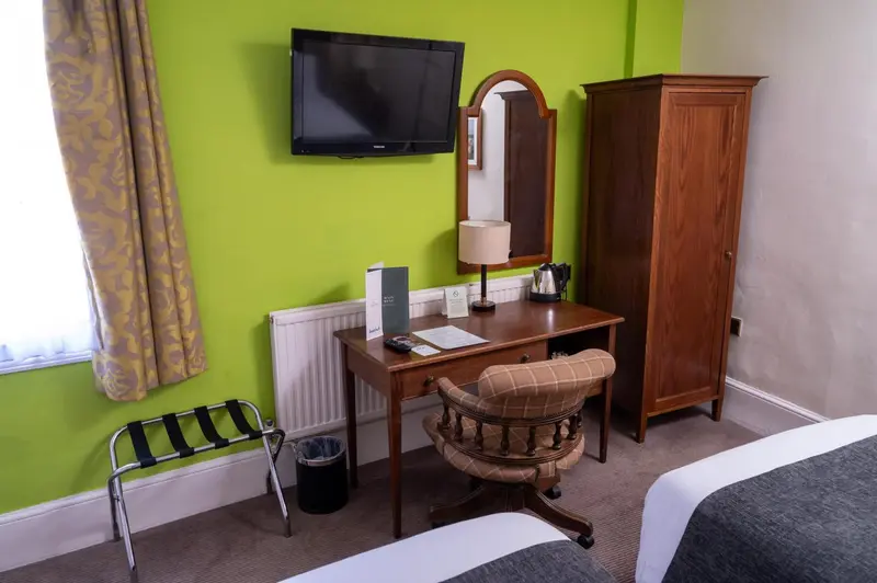 Une chambre lumineuse avec un bureau en bois et un téléviseur mural.
