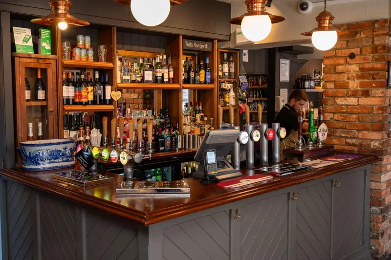 Un comptoir de bar en bois sombre est garni de bouteilles et de verres.