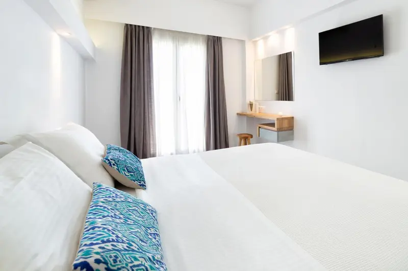 Une chambre lumineuse avec un lit blanc et des coussins bleus.