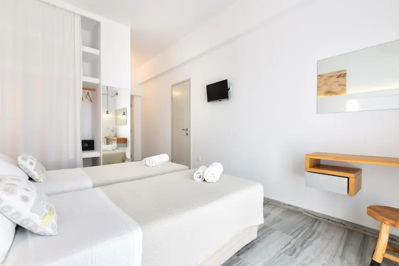Une chambre lumineuse avec deux lits simples et un téléviseur mural.