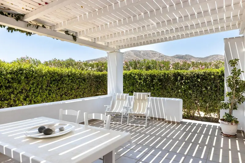 Terrasse ombragée avec mobilier blanc et vue sur la végétation et les montagnes.