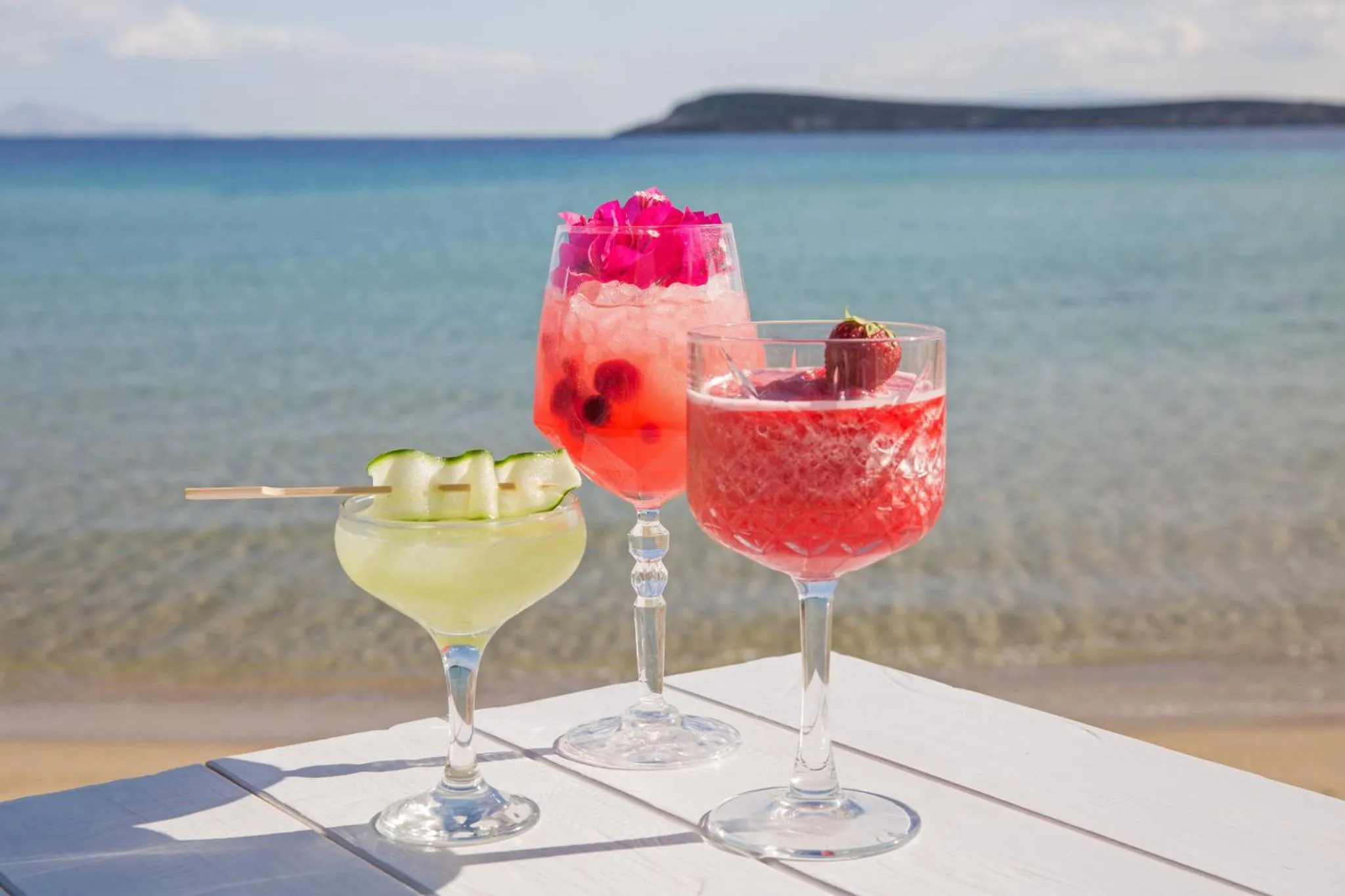 Trois cocktails colorés sont présentés sur une table en bord de mer.