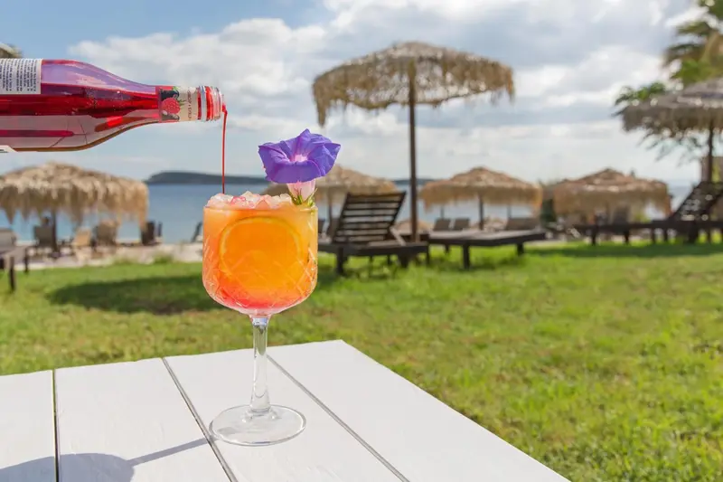 Un cocktail coloré est servi sur une table en bois face à la mer.