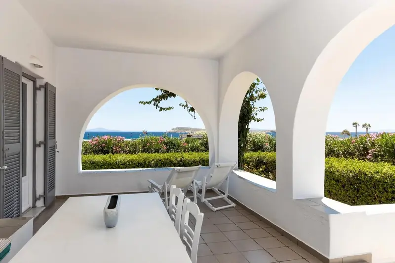 Terrasse blanche avec table et chaises donnant sur la mer.