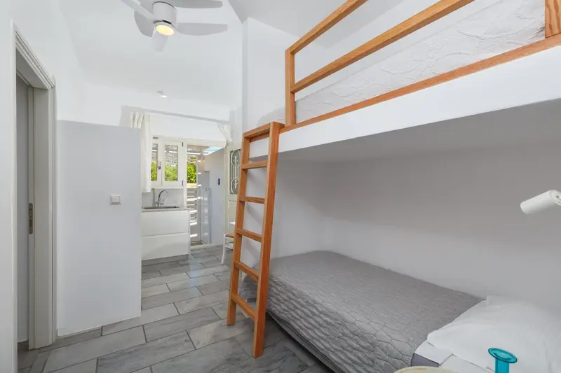 Une chambre lumineuse avec un lit superposé et une kitchenette en fond.