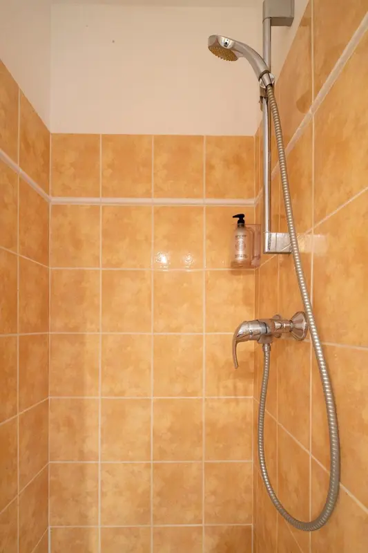 Douche murale avec pommeau et robinetterie chromées sur fond de carrelage ocre.