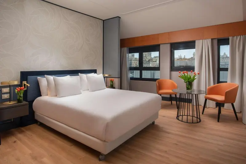 Une chambre lumineuse avec un grand lit et deux fauteuils.