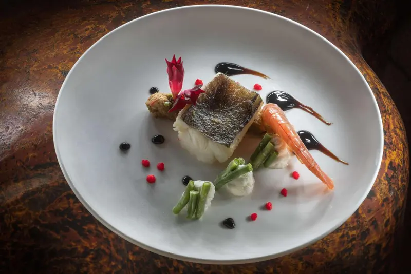 Assiette de poisson blanc accompagnée de légumes et d'une sauce décorative.
