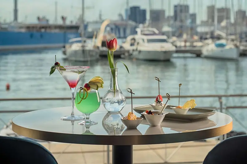 Une table ronde présente des boissons colorées et des amuse-gueules en bord de mer.