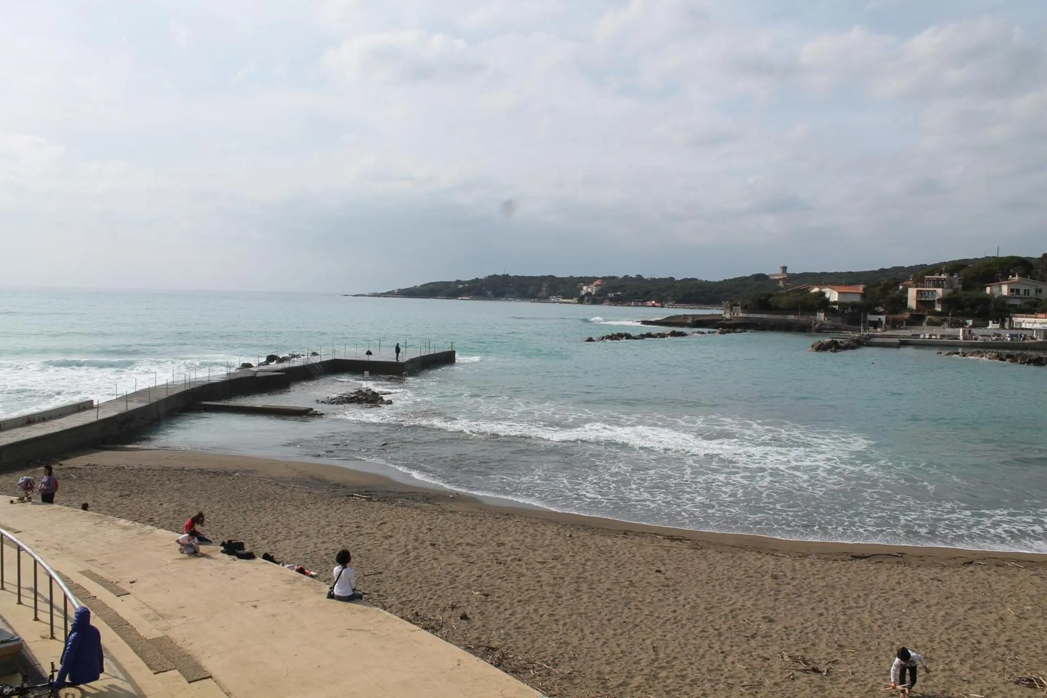 Une plage de sable avec des personnes assises et une vue sur la mer.