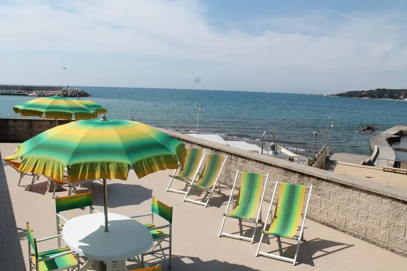 Terrasse ensoleillée avec parasols colorés et chaises longues face à la mer.