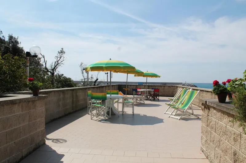 Terrasse ensoleillée avec mobilier de jardin et vue sur la mer.