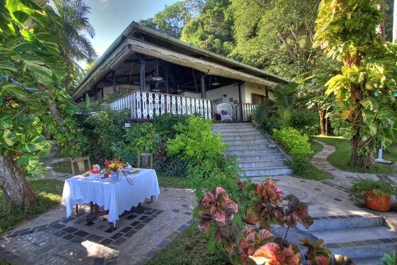 Une table dressée sur une terrasse ensoleillée devant un bâtiment verdoyant.
