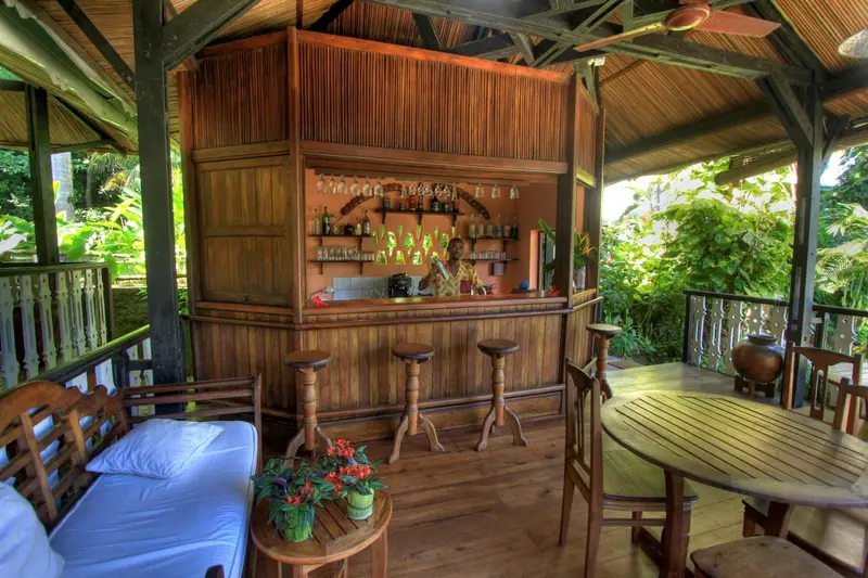 Un comptoir de bar en bois est installé dans une structure ouverte sur une végétation luxuriante.