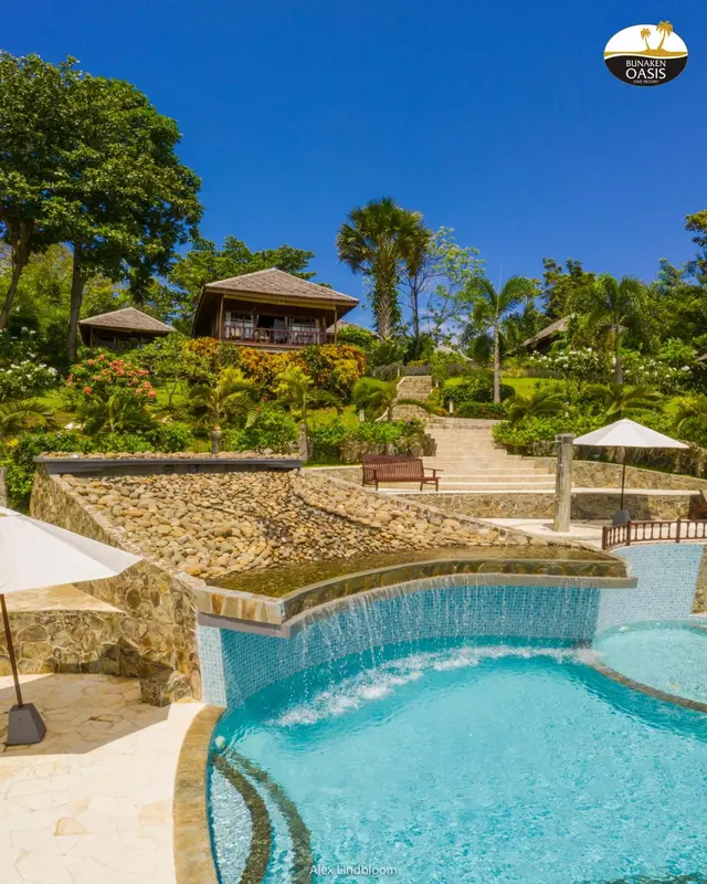 Une piscine avec une cascade et des transats sur une terrasse ensoleillée.