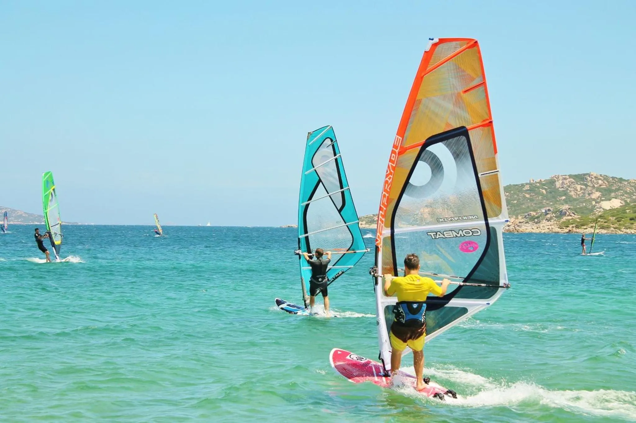 Des pratiquants de planche à voile naviguent sur une eau turquoise.