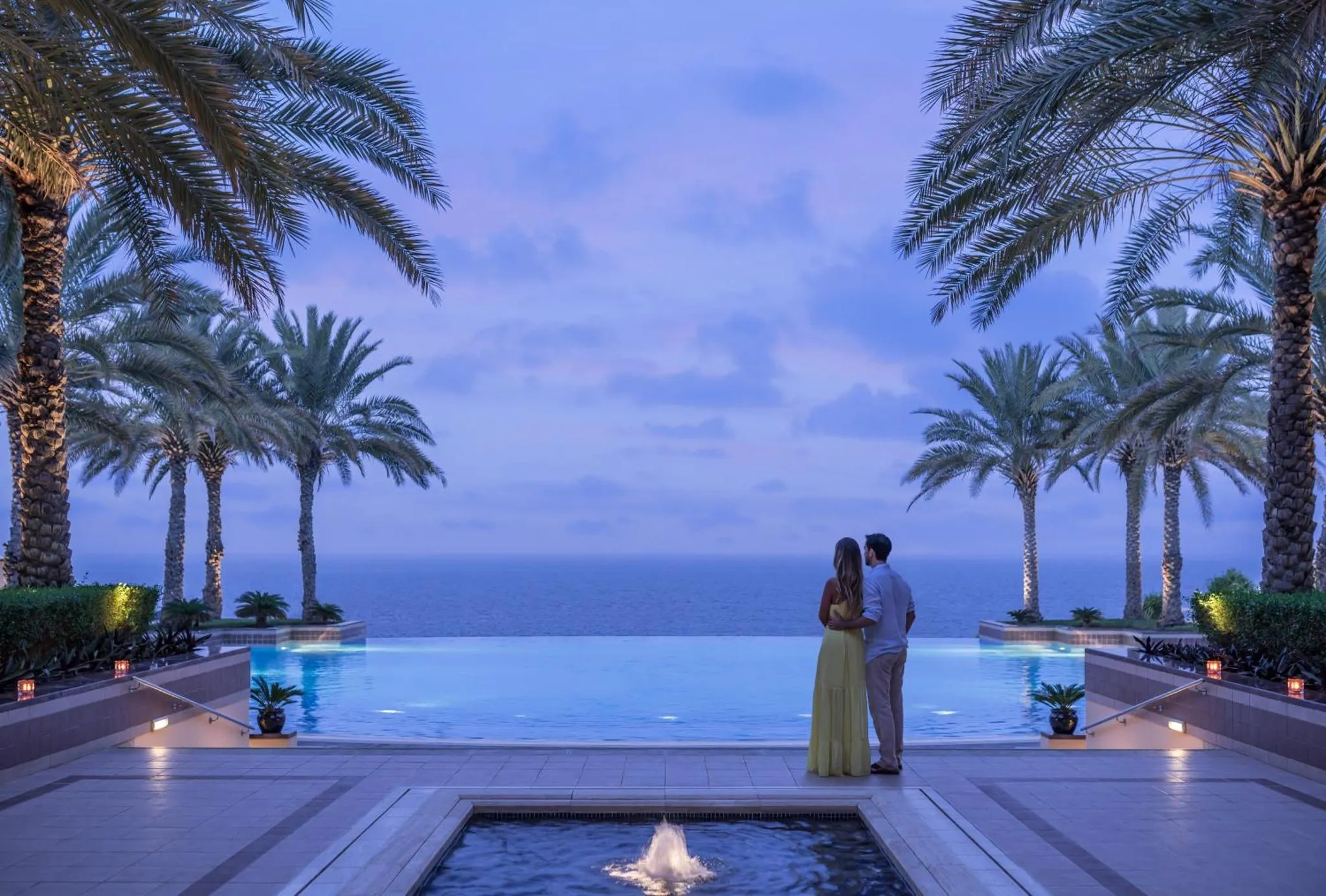 Un couple se tient près d'une piscine à débordement avec vue sur la mer au crépuscule.