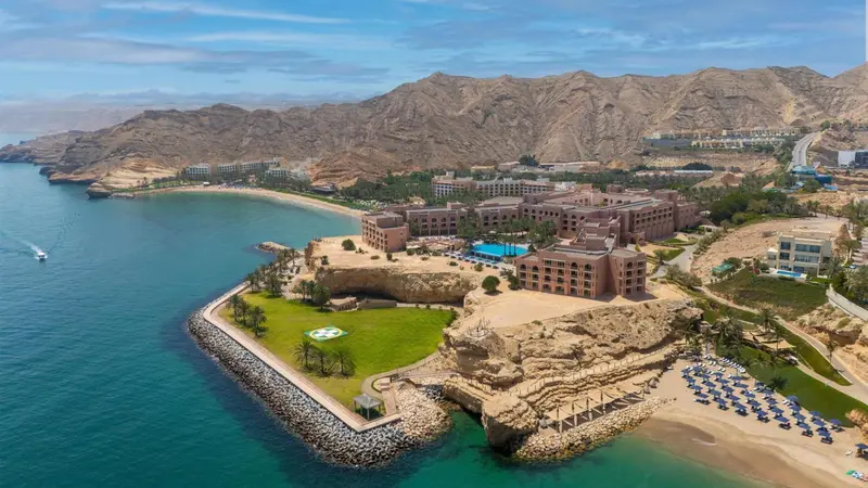 Vue aérienne d'un complexe hôtelier bordant une plage et une baie rocheuse.